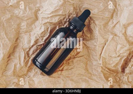 CBD-Ölflasche, Hyaluronsäure-Tinktur auf gefaltetem Karton. Serum mit Kollagen und Peptiden auf zerknittertem Papier. Mockup für Schönheitsprodukte. Amt Stockfoto