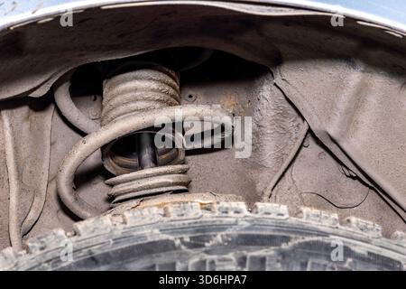 Gerissene Gummi- oder Kunststoffmanschette, die Stoßwelle und Feder freilegt, weist auf vorzeitigen Verschleiß durch raue Fahrbedingungen hin. Selektiver Fokus Stockfoto