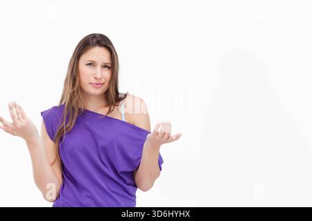 Frau, die im Studio steht und zuckt, verwirrt im Gesicht und trägt ein violettes, schulterfreies Oberteil mit sichtbarem BH-Riemen. Verwirrt, Gesten, Hochformat, weiß, Hintergrund, cas Stockfoto