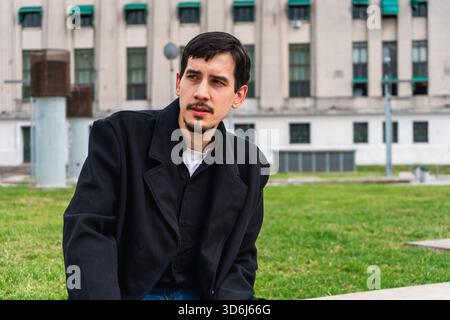 Junger Mann, der in einem Stadtpark sitzt, wegschaut und denkt. Besinnung, Besinnung und Einsamkeit in der Stadt Stockfoto