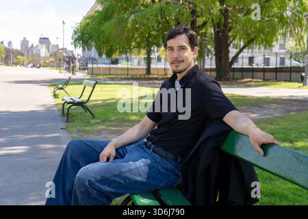 Junger Mann, der sich auf der Parkbank entspannt und lächelt Stockfoto