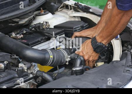 Fokussierter Mechaniker, der während der Reparatur den Motor des Autos anspricht. Kfz-Service- und Wartungskonzept, das professionelle Techniker bei der Arbeit in der Garage zeigt Stockfoto