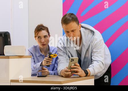 Mitarbeiter, der mit einem Strichcode-Lesegerät das mobile Gerät des Patrons an der Abholstation scannt Stockfoto