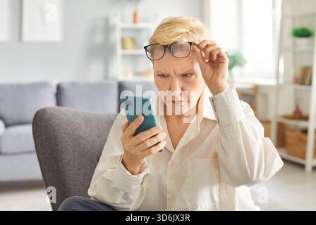 Ältere Frau, die zu Hause auf dem Sofa sitzt und ihr Smartphone nutzt, um soziale Medien im Internet zu durchsuchen. Stockfoto