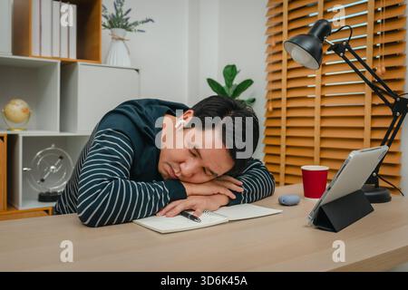 Müder Mann mit Tablet und schnurlosen Ohrstöpseln im Home Office Stockfoto