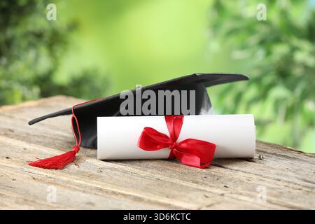 Graduierungskappe und Diplom auf Holztisch vor verschwommenem Hintergrund, Nahaufnahme Stockfoto