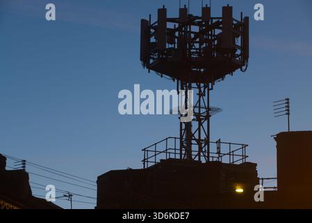 Ein Handymast steht in Silhouette vor einem klaren Morgenhimmel, dessen Antennen und Metallrahmen im weichen Morgenlicht scharf umrissen sind. Stockfoto