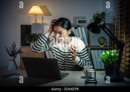 Stressige Frau mit Laptop und schnurlosen Ohrstöpseln, die nachts Videoanrufe tätigen Stockfoto