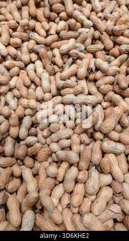 Redaktionelle Nahaufnahme von ungeschälten Erdnüssen, die einen dichten texturierten Hintergrund bilden. Das Foto hebt natürliche Muster hervor. Stockfoto