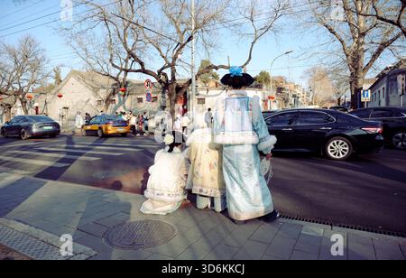 Frauen in traditionellem Hanfu warten in einem Hutong in Peking am Straßenrand und beobachten Autos, die an einem frischen Winternachmittag vorbeifahren Stockfoto