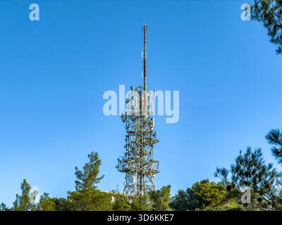 Telekommunikationsmast über Wald unter klarem blauem Himmel Stockfoto