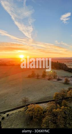 Goldener Sonnenaufgang über frostigen Feldern mit weidenden Schafen und fernen Hügeln an einem klaren Wintermorgen in der schottischen Landschaft in Criefff Stockfoto