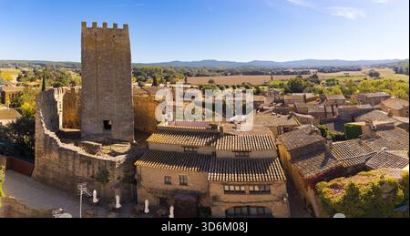 Panoramablick auf Peratallada mit dem mittelalterlichen Schlossturm, der sich über gekachelten Dächern erhebt, umgeben von einer Landschaft unter einem klaren blauen Himmel. Stockfoto