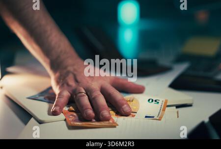 Handgriff Auf Euro-Banknoten. Schnelle männliche Handbewegung über verstreute Euroscheine, die auf dem Schreibtisch mit Dokumenten und Notizbuch bei schlechten Lichtverhältnissen liegen Stockfoto
