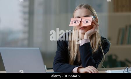 Humorvolle kaukasische Geschäftsfrau mit Haftnotizen auf den Augen Brille am Tisch mit Laptop gefälscht Arbeit im Büro Geschäftsfrau weibliches Mädchen lustig Stockfoto