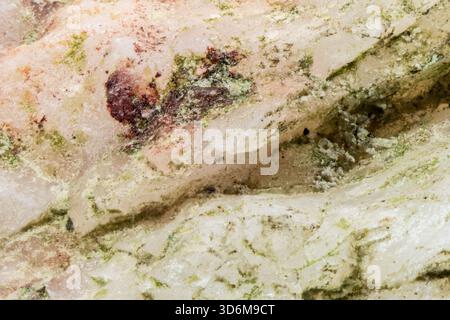 Makronaht von weißem Marmorgestein mit grünen Mineraladern und rötlichen Einschlüssen Stockfoto