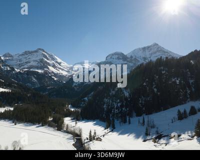 Sonnendurchflutete, schneebedeckte Schweizer Alpen und Kiefernwald über dem Lauenensee Stockfoto