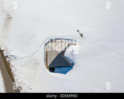 Aus der Vogelperspektive einer isolierten Almhütte auf einer schneebedeckten Landschaft mit sichtbaren Wanderwegen Stockfoto