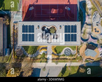 Blick aus der Vogelperspektive auf den Kindergarten in Ittigen mit Innenhof auf der Dachterrasse, Solarpaneelen und farbenfrohem Spielplatz Stockfoto