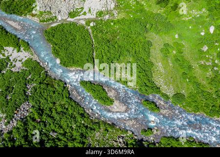 Blick aus der Vogelperspektive auf den Turquoise Glacial River, der sich durch ein üppiges Alpental schlängelt Stockfoto