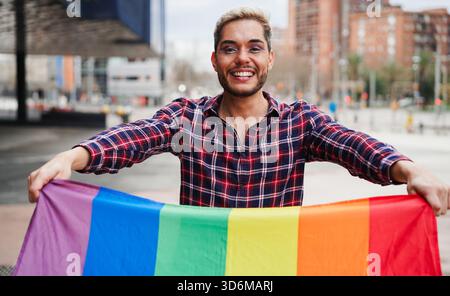 Junger schwuler Mann mit Make-up, der Spaß hat, lgbt-Regenbogenfahne draußen zu halten - gleiche Rechte für homosexuelle Menschen und lgbtq-Konzept - Fokus auf Gesicht Stockfoto