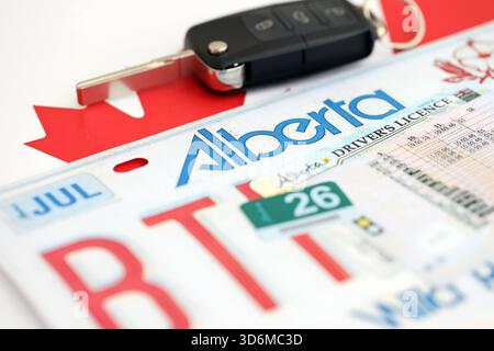 Alberta canadian Autokennzeichen und Zündschlüssel auf der Flagge von Kanada Nahaufnahme. Führerschein- und Zulassungskonzept Stockfoto