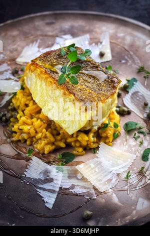 Gebratenes Fischfilet aus nordischem Kabeljau mit safran-Risottoreis, grünem Gemüse und Parmesankäse Stockfoto