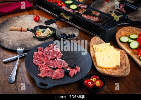 Traditionelles, authentisches schweizer Raclette mit Rindfleisch, Gurken, Savoyenkäse und Gemüse Stockfoto