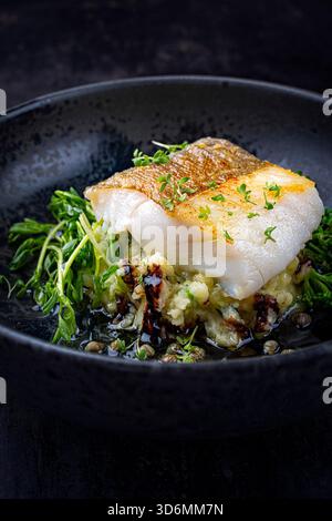 Frittiertes nordisches Fischfilet aus Dorsch mit Kartoffelpüree, grünem Gemüse und Balsamico-Essig in Umami-Fischsauce Stockfoto