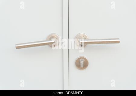 Weiße Türverkleidung oder Türblatt mit zwei silbernen Türgriffen oder Griffen und separatem Schlüsselloch wird als Hintergrund verwendet. Stockfoto