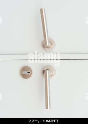 Weiße Türverkleidung oder Türblatt mit zwei silbernen Türgriffen oder Griffen und separatem Schlüsselloch wird als Hintergrund verwendet. Stockfoto