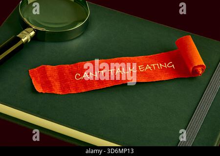 Eine orangefarbene Papierrolle mit dem Satz kann nicht reden Essen ruht auf einem dunkelgrünen Journal. Stockfoto