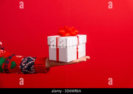 Kinderhände präsentiert ein umhülltes Geschenk mit roter Schleife, perfekt für festliche Werbung, Produktaktionen, saisonale Kampagnen und Weihnachtsgrafiken Stockfoto