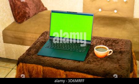 Laptop-Modell mit grünem Bildschirm und Kaffee auf gemütlichem Tisch Stockfoto