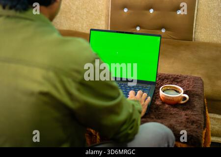 Mann, der auf einem Green-Screen-Laptop mit Kaffee in einem komfortablen Zuhause arbeitet Stockfoto