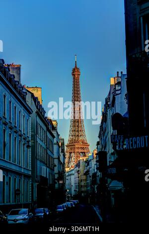 Der Eiffelturm wurde bei Sonnenaufgang zwischen Pariser Gebäuden eingerahmt, von einer schmalen Straße aus gesehen, in der die Eisenkonstruktion ein warmes frühes Licht erstrahlt. Stockfoto
