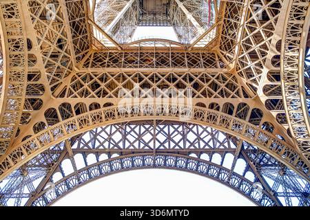 Nahaufnahme der eisernen Gitterstruktur des Eiffelturms mit warmem Morgenlicht vor einem klaren blauen Himmel in Paris, Frankreich. Stockfoto