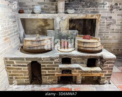 Alte Holzbrennküche Nachbildung mit Backsteinofen, großen hölzernen Töpfen und Töpfertopf, vor einer Backsteinmauer im Dorf Zili. Zeigt das traditionelle Kinn an Stockfoto