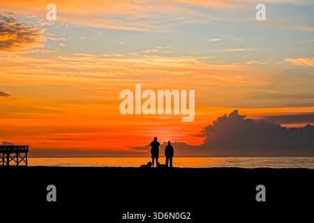 Isle Of Palms, Usa. November 2025. Ein Paar mit ihren Hunden, umgeben vom Sonnenaufgang über dem Atlantik am Front Beach, 21. November 2025 in Isle of Palms, South Carolina. Quelle: Richard Ellis/Richard Ellis/Alamy Live News Stockfoto
