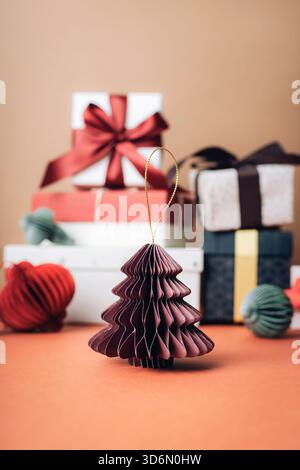Ein kleiner gefalteter Papierbaum, der vor gewickelten Geschenken und Bändern platziert wird, sorgt für eine weihnachtliche Weihnachtsszene mit warmen Tönen. Nahaufnahme. Stockfoto
