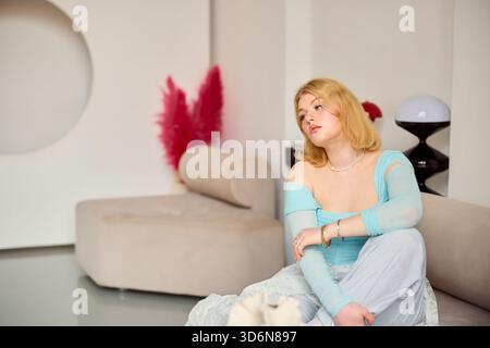 Junge Frau, die in einem modernen Zimmer mit stilvoller Einrichtung und sanften Farben sitzt Stockfoto