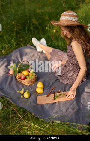Frau, die ein Picknick mit frischem Obst auf einer sonnigen Wiese genießt Stockfoto