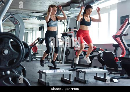Zwei Frauen in Sportbekleidung springen im Fitnessstudio auf der Plattform Stockfoto