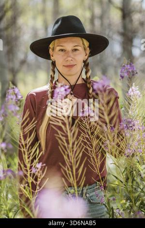 Eine Frau mit Zöpfen, die Cowboyhut trägt, steht inmitten von Wildblumen Stockfoto