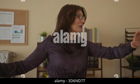 Frau in lila Bluse und Brille zeigt mit dem Finger neben Korkbrett im Bürogebäude; Entschlossenheit. Stockfoto