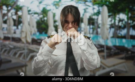 Pilotin in Uniform, die am Pool des Resorts spielerisch im Freien boxt, Beruf und Freizeit in einem lebhaften Hotel vereint und die Abschreckung zum Ausdruck bringt Stockfoto