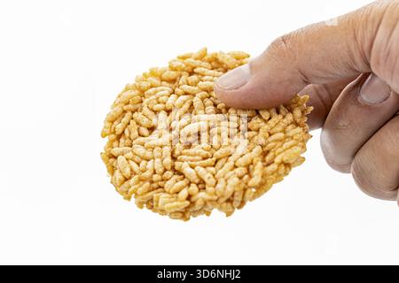 Eine Nahaufnahme einer Hand, die einen runden, strukturierten Puffreis-Snack vor einem sauberen weißen Hintergrund hält und die knusprige und leichte Natur des Tres unterstreicht Stockfoto