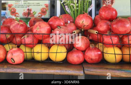 Frische Granatäpfel und Orangen sind in Drahtkörben an einem belebten Straßenstand angeordnet, die farbenfrohe Früchte und eine geschäftige Marktatmosphäre hervorheben Stockfoto