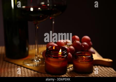 Stillleben zwei Weingläser mit Traubenstrauß in der Nähe romantischer Aromen brennende Flammenkerzen auf einem Tisch auf dunklem Hintergrund. Dekorkonzept von Weihnachten Stockfoto