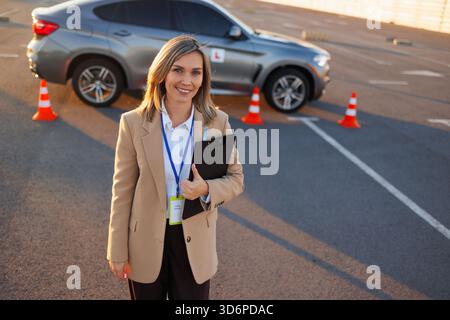 Lächelnder Fahrlehrer mit Klemmbrett in der Nähe des Fahrstuhls auf dem Testgelände Stockfoto